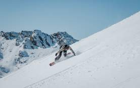Spring snowboarder shredding a slope at The Remarkables with blue sky and mountains in the background