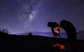 Person with telescope stargazing underneath the milky way near The Remarkables mountain range