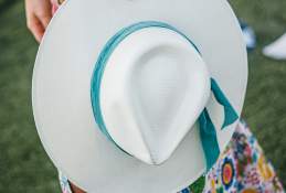 Close-up of a girl's hand holding a tan hat with a teal velvet ribbon