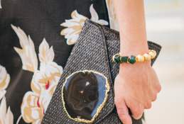 Close up shot of a hand holding a black jeweled clutch and wearing a gold and green bracelet