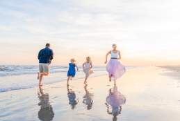 A family of four in pastel colors runs on the beach at sunrise