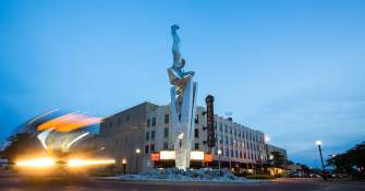 White tall statue with theater in backgound and lights from car blurred on left side