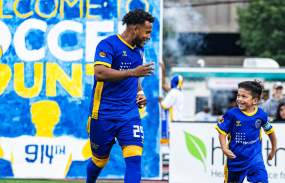 A Westchester Soccer Club player runs out onto the field accompanied by a youth player.