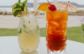 Two cocktails are on a table. In the background is an arch-shaped piece of artwork and the Hudson River in the distance.