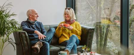 Older couple sitting on coffee shop sofa drinking cups of coffee