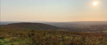 A rural Welsh landscape with the sea in the distance and a low sun in the sky.