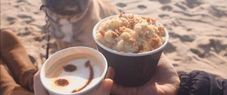 couple and their dog sitting on the beach with coffees