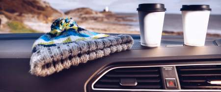 two coffee cups and a bobblehat on a car dashboard