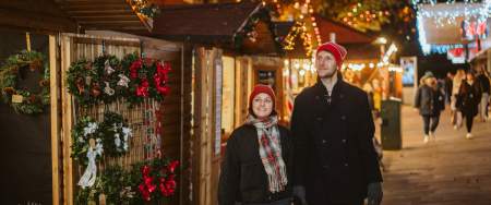 Young couple holding hands and exploring Swansea Christmas Market at night