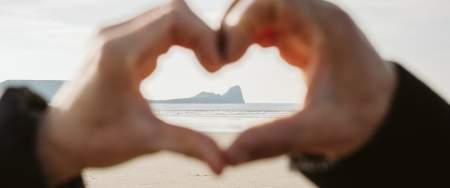 A close up of a pair of hands making a heart shape with Worm's head visible in the distance in the centre of the heart shape.
