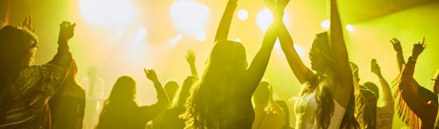 People dancing with their arms in the air in yellow light
