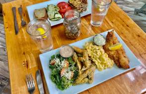 two plates of food on a table - fish, mac and cheese, fries, greens
