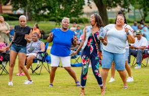 Four people dancing outdoors in front of a crowd of people