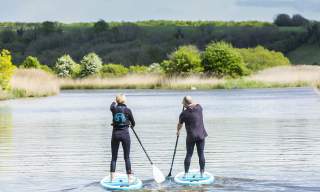 A couple stand up paddle boarding along a river in Sussex