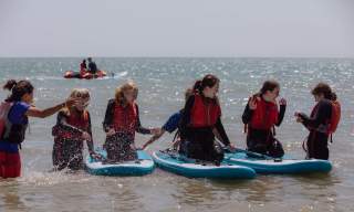 A group of young people wearing red life vests sit on paddleboards in the sea at Eastbourne