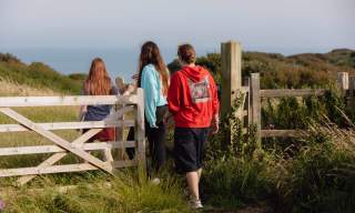 A group of 3 young people walking through a gate towards the sea on the Sussex Downs