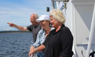 En mann og to kvinner står ved relingen på en båt og peker ut mot havet