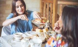 A woman in a blue dress takes a scone from a cake stand, which is filled with sandwiches, scones and cakes, in the Cotswolds