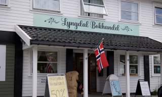 Inngangspartiet til Lyngdal Bokhandel med norsk flagg og tilbudsskilt.