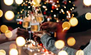 A group of people clink champagne flutes surrounded by twinkling Christmas lights
