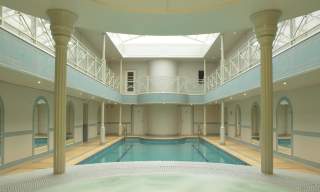 View from a hot tub of a rectangular pool surrounded by arched mirrors and ornamental pillars, with a mezzanine balcony above. The Lygon Arms Spa in the Cotswolds