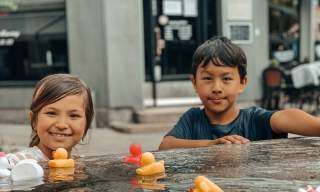 To små barn som leker med plastikk-badeender i vannskulpturen Flod. Foto.