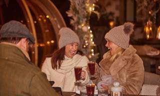 Two ladies in bobble hats enjoying mulled wine at a Christmas market at Wild Thyme and Honey