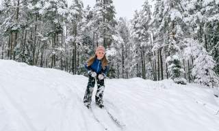 Barn som står på ski ned en bakke i skogen. Foto.