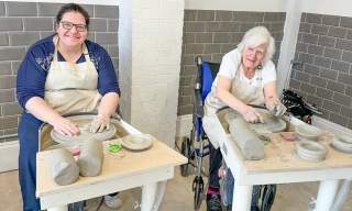 A wheelchair user and friend at Honeybourne Pottery using a potters wheel