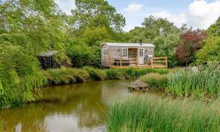 View across a pond to a wooden glamping caravan