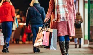 Lady dressed in light pink jacket and scarf carrying a bundle of Christmas shopping