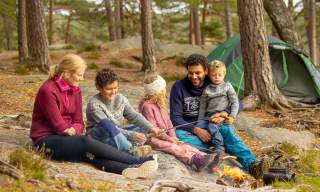 Familie på tur i skogen hvor de griller pølser.