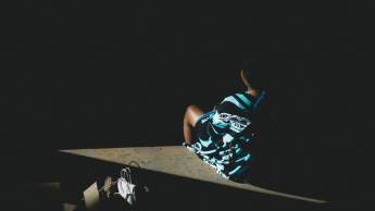 A child wearing a shirt with traditional Coast Salish artwork sits quietly in a shaft of sunlight inside a dimly lit wooden hall.