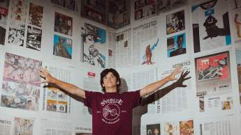 A person standing with their arms out in front of a wall covered in newspaper.