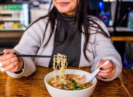 woman smiling while using chopsticks to eat a bowl of ramen
