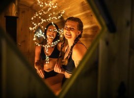Looking through a sauna window at two women smiling.
