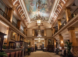 Grand hotel lobby with ornate chandeliers, marble columns, and a painted ceiling mural, creating an elegant and historic atmosphere.
