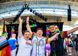 three friends cheering in front of a stage at pridefest