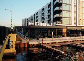 Waterfront view of The Bridgewater restaurant and apartments in Milwaukee, with outdoor dining and boats docked along the river