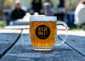 A large beer is set upon a wood table with blurred umbrellas in the background.
