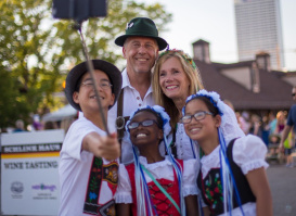 a family taking a selfie with a selfie stick in traditional German attire on festival grounds