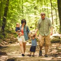 A family of 4 hikes through the woods on an easy trail at Paris Mountain State Park.