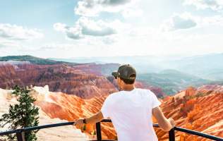 Person standing at scenic overlook at Cedar Breaks National Monument with a red rock canyon in the background and blue skies.