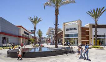 Outlets at Orange in Orange County, California, featuring shoppers strolling through an open-air retail center with palm trees, a central fountain, popular outlet stores, and sunny Southern California weather.