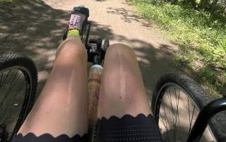 Wide natural trail with trees and grasses on each side. A recumbent quad cycle is biking down the path.