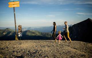 A happy family hiking on top of a mountain with ski trail sign markings