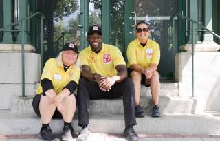 Three people sitting on steps wearing yellow downtown ambassadors shirts