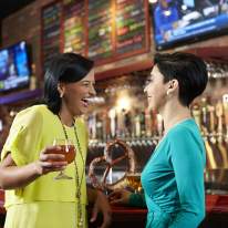 Two women in pastels eat pretzels at world of beer in the mall surrounded by faux brick, taps and televisions