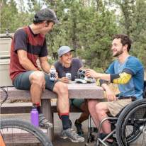 Three friends sitting around a park bench having a beer after biking together.