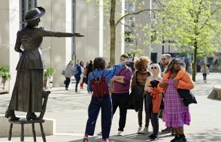 Tour group stood in square in Manchester with a guide in front of Emmeline Pankhurst statue